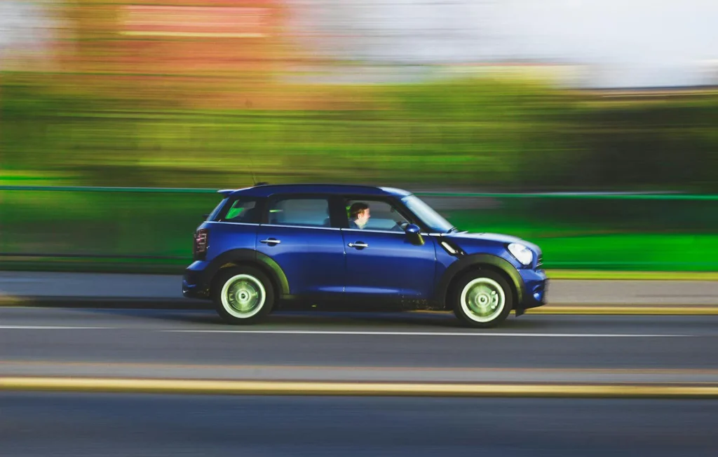 In the image a blue car speeds on a road. The background is blurred.