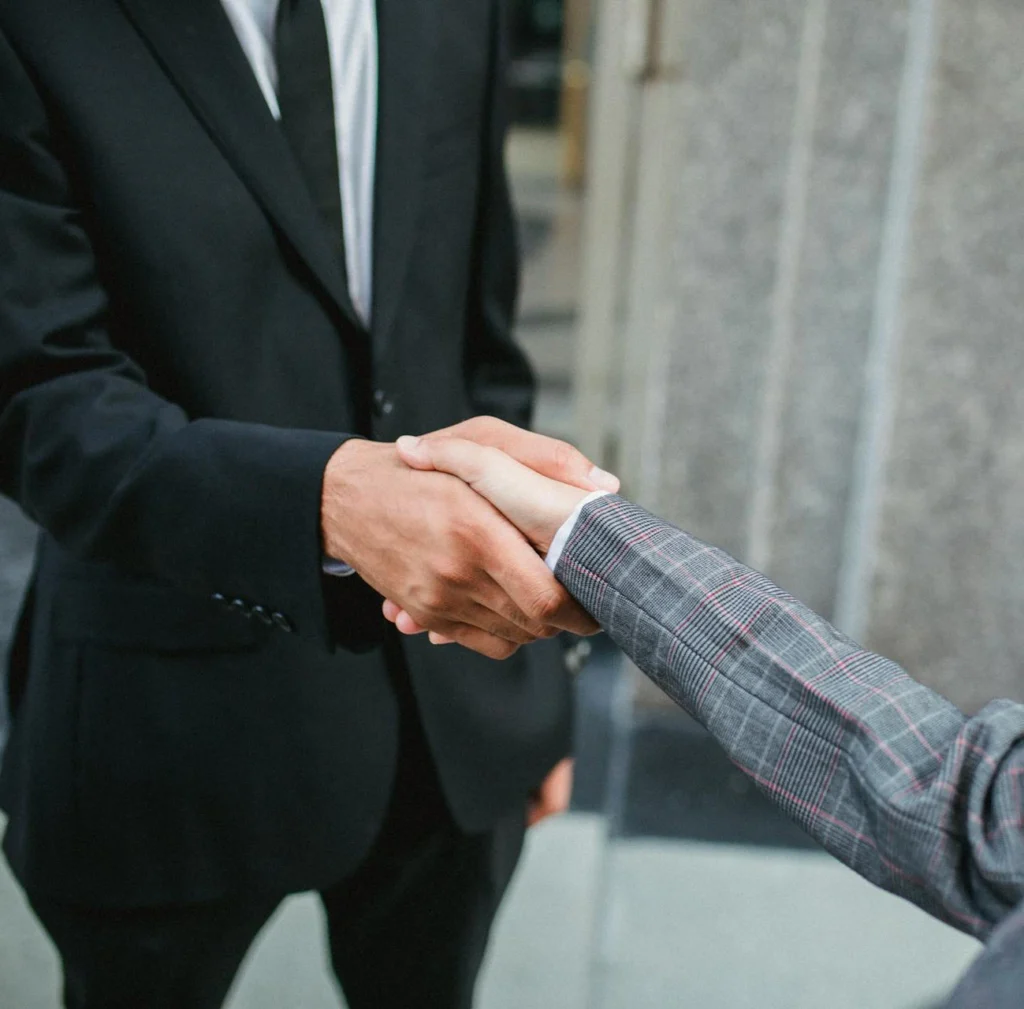 In the image a man and a woman dressed in formal business clothes shake hands